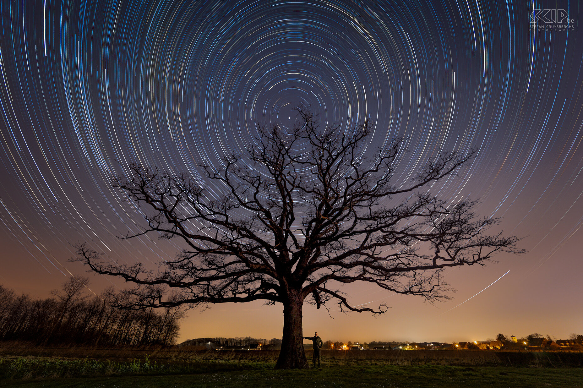 Hageland by night - Oude eik van Kaggevinne met sterrensporen Een selfie met sterrensporen aan de oude eik van Kaggevinne vlakbij mijn thuis in Scherpenheuvel-Zichem. Dit beeld is gemaakt door het samenvoegen van 240 beelden met telkens een belichting van 30 seconden. Recht boven deze prachtige eik staat de poolster waarrond de andere sterren lijken te draaien (in werkelijkheid draait de aarde natuurlijk). Stefan Cruysberghs